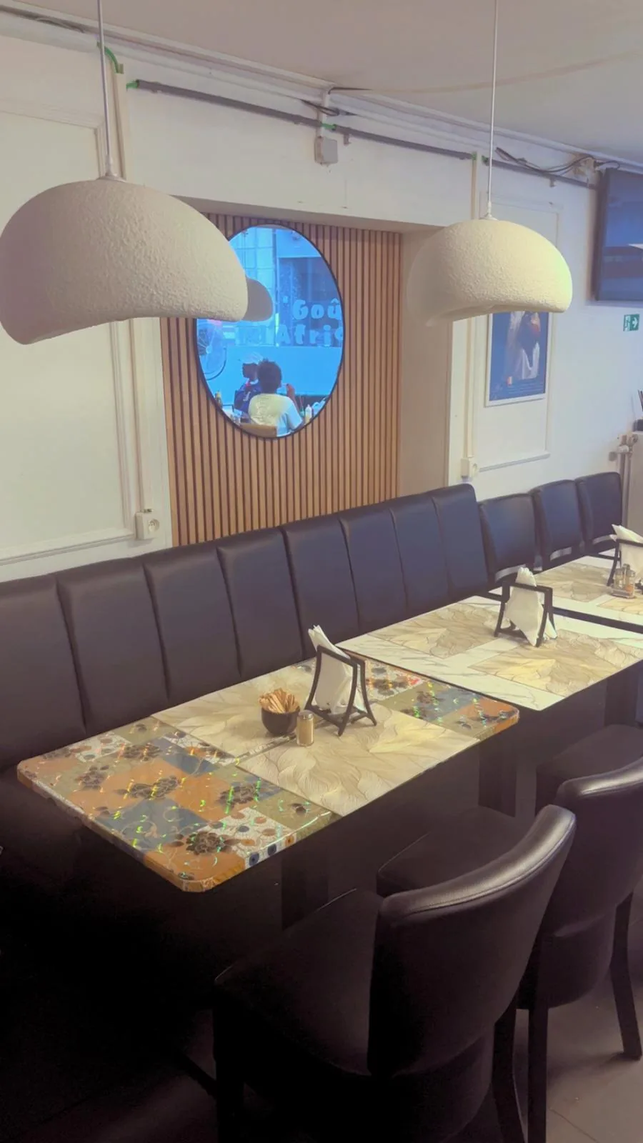 Salle du restaurant : banquette, tables dressées et miroir rond